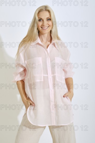 A woman stands confidently in a bright studio, wearing a light pink oversized shirt with pockets