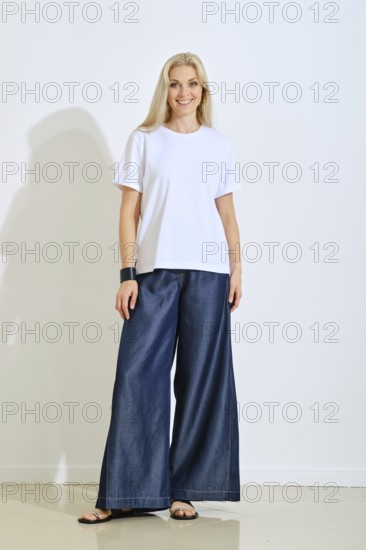 A smiling woman stands confidently in a bright studio space, wearing a simple white t-shirt and