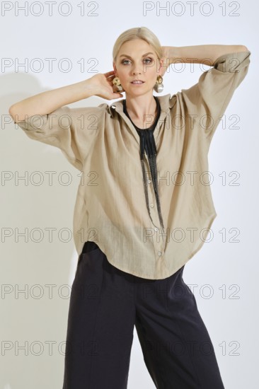 A woman strikes a confident pose while wearing a chic beige shirt complemented by bold accessories.