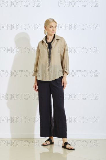 A model stands confidently in a bright studio space wearing a stylish beige top and black wide-leg