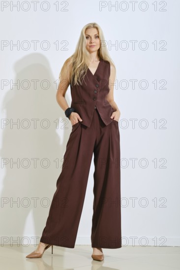 A model stands confidently in a brown vest and matching pants. Her long hair flows down as she