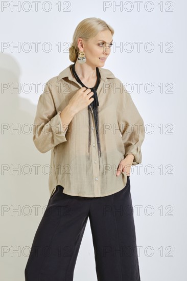 A woman stands gracefully in a modern studio, wearing a light-colored casual shirt and dark pants.