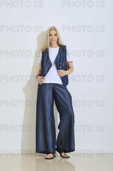 A woman stands confidently in a fashionable outfit consisting of a navy vest over a white shirt and