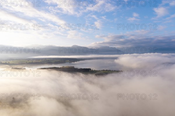 Morning fog hovers over Lake Forggensee with mountains in the background, near Rosshaupten,