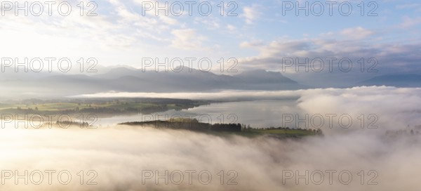 Foggy landscape with view of Lake Forggensee and mountain skyline in the background, near