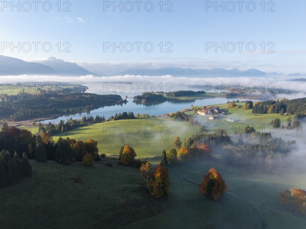 Early autumn morning landscape with idyllic Forggensee and picturesque hills surrounded by fog,