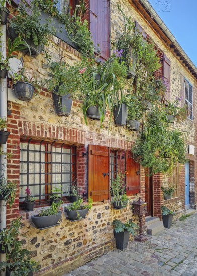 A quaint old masonry building with wooden shutters, adorned with numerous planters overflowing with