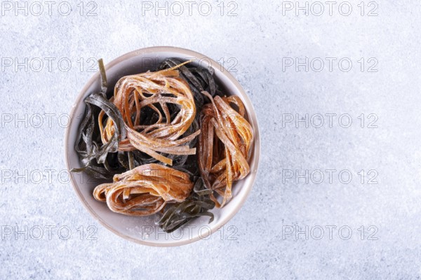 Pasta with carrots and spinach in a round plate on a light textured background, top view, space for