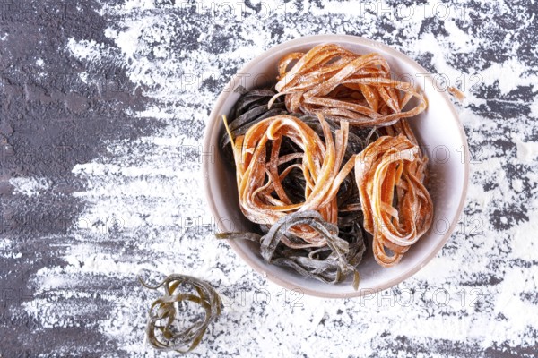 Pasta with carrots and spinach in a round plate on a table covered with flour, top view, space for
