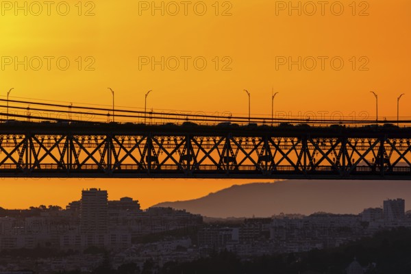 Bridge spans city skyline, silhouetted against vivid orange sunset. Soft city outlines and distant
