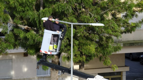 Two unrecognizable utility workers operate hydraulic lift to repair street light in residential