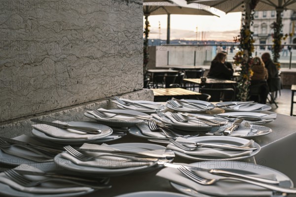 Plates neatly arranged with forks, knives, and napkins on stone countertop at outdoor restaurant in