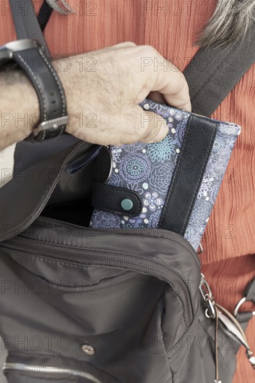 Pickpocket thief Person's hand storing a distinctive floral pattern wallet in a dark-colored