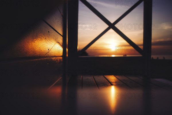 A warm sunset over the sea viewed through a wooden structure with visible reflections. Sea, Baltic,