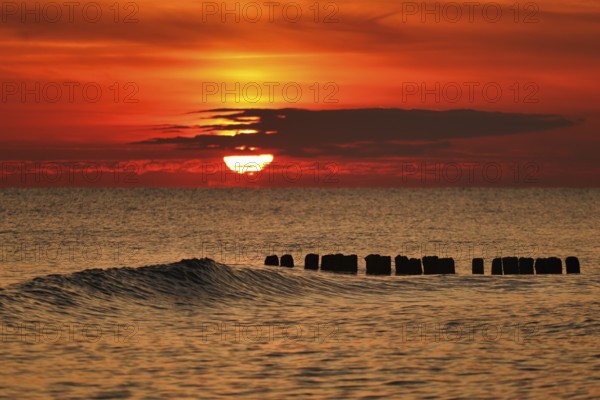 A vivid sunset over the sea with gentle waves and an orange sky creating a tranquil atmosphere.