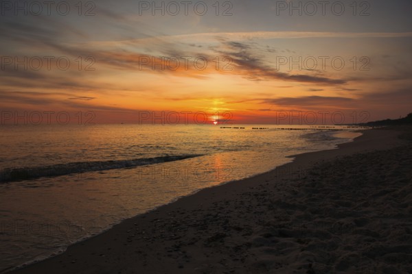 A serene sunset over the sea with golden skies and gentle waves lapping at the sandy beach. Sea