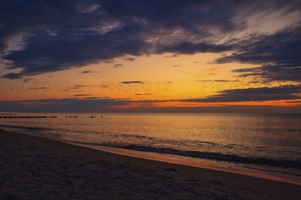 A tranquil beach sunset with vibrant colors in the sky and gentle waves lapping at the sandy shore.