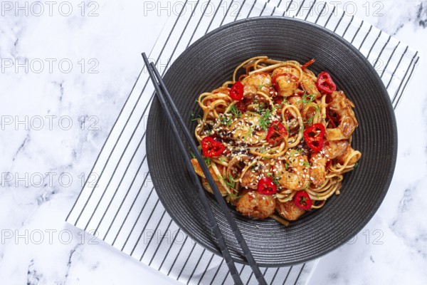 Delicious shrimp stir-fry with noodles and colorful vegetables served in a black bowl on a striped