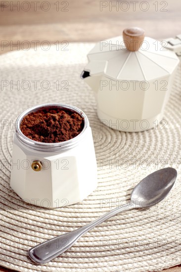 Geyser coffee maker with ground coffee and a spoon on the background of a woven rug, coffee