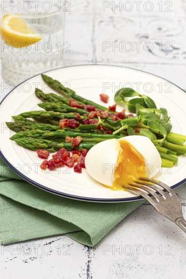 Poached egg with fork, asparagus, bacon slices and herbs, on a white plate, breakfast, close-up, no