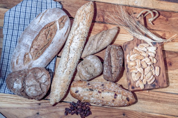 Freshly baked artisanal bread loaves, baguettes, and rolls on a wooden surface with wheat ears and