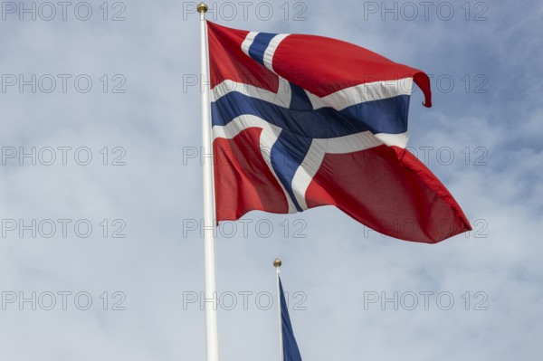 The national flag of Norway fluttering against the blue sky and gentle clouds. Oslo, Østlandet,