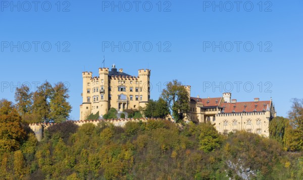 The majestic Hohenschwangau Castle towers over a colorful autumn landscape under clear blue sky,