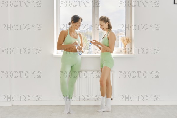 Two women pause during their fitness stretching class in a bright and spacious studio. They are
