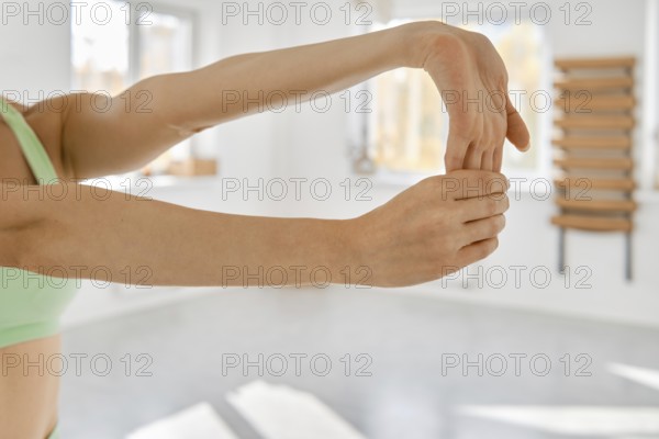 A person is performing a wrist stretch in a well-lit fitness studio. The individual extends their