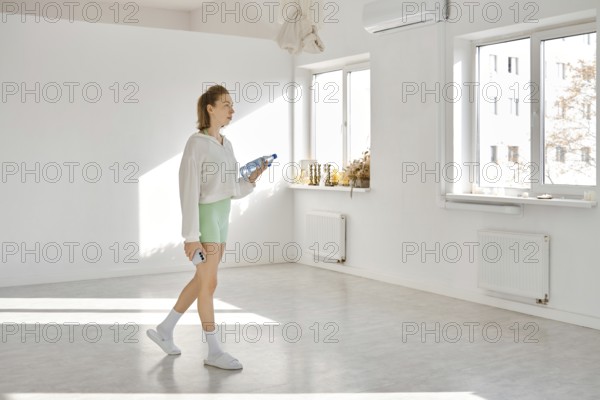 In a bright studio with white walls and sunlight streaming through large windows, a young woman
