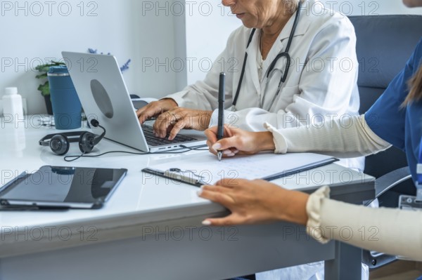 Medical team composed of a doctor and a nurse working together on patient files, with one typing on