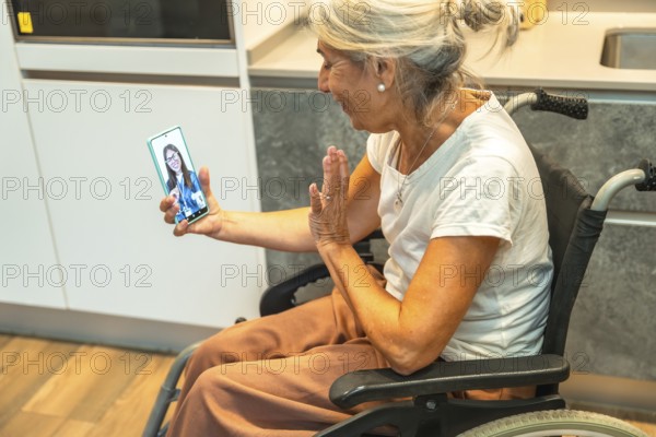 Senior woman in a wheelchair laughing and waving during a video call on her smartphone, connecting