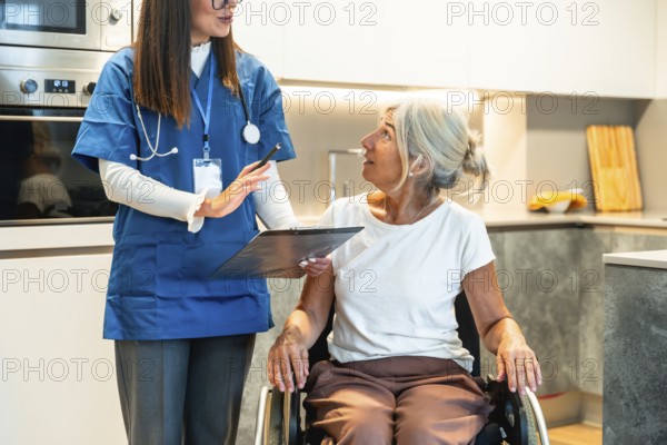 Nurse reviewing a healthcare plan with an elderly woman in a wheelchair in a modern kitchen,