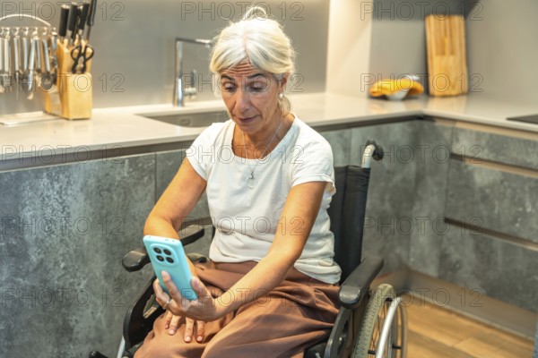 Senior woman in a wheelchair video calling on a smartphone from a modern kitchen, engaging in