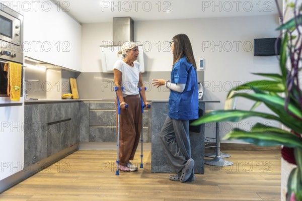Home caregiver interacting with a senior woman using crutches, providing support and advice for her