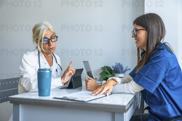 Experienced doctor discussing treatment with a smiling young nurse, both utilizing digital tablets