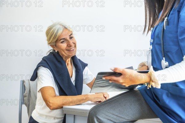 Senior woman smiling and listening as doctor in blue scrubs reviews a medical chart, sharing a
