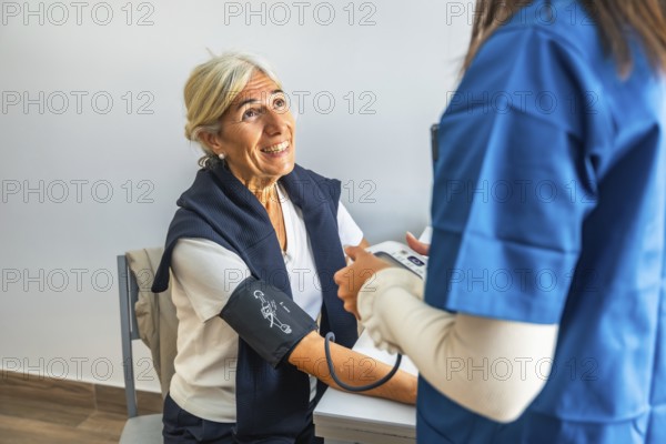 Nurse measuring blood pressure of smiling elderly woman during routine clinic checkup, highlighting