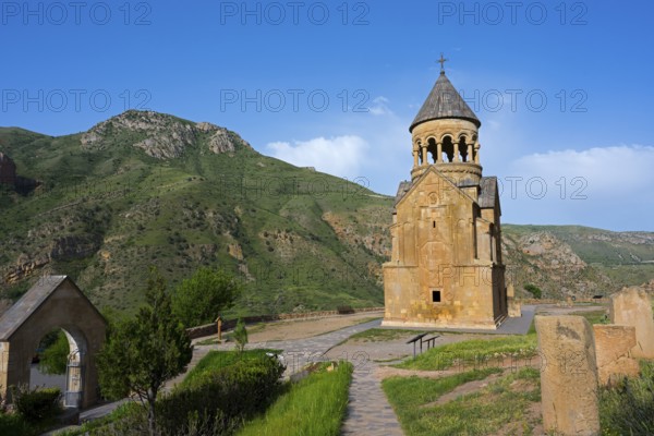 A chapel against a green mountain landscape under a blue sky, surrounded by nature, Noravank