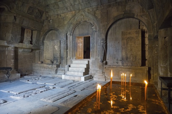 Ancient stone room with candles and grave plaques creating a calm and mystical atmosphere, Noravank