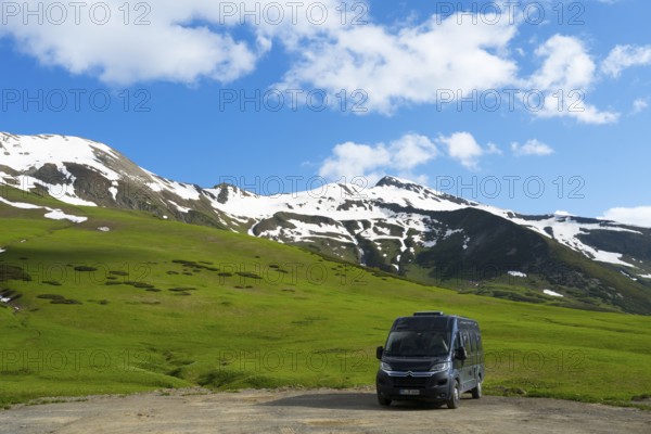 A motorhome stands in front of a green, snow-covered mountain landscape under a blue sky, Camper,