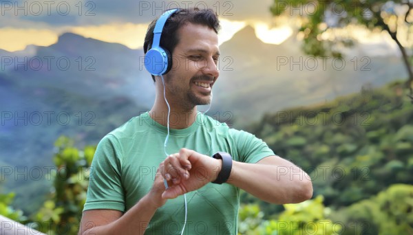 A man wearing headphones and a green shirt is smiling and looking at his watch. He is wearing a