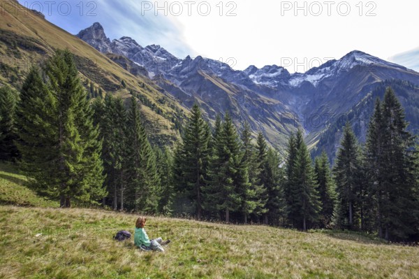 Young woman sitting in a meadow and looking at the mountains of the Allgäu Alps with