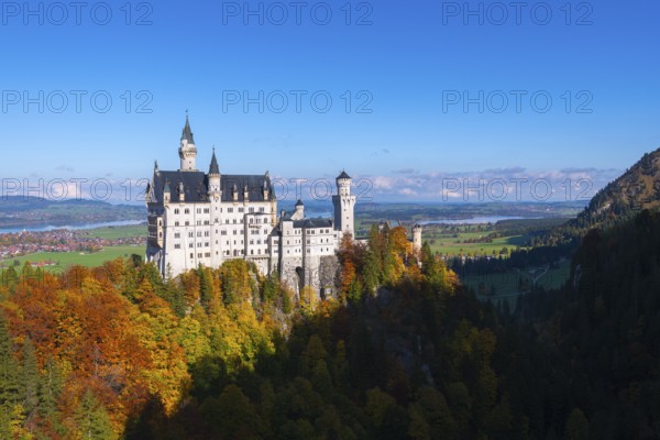 Fairytale castle Neuschwanstein on a wooded hill surrounded by autumnal splendor under wide skies,