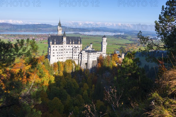 Neuschwanstein Castle on a wooded hill overlooking a green landscape with a wide panorama and blue
