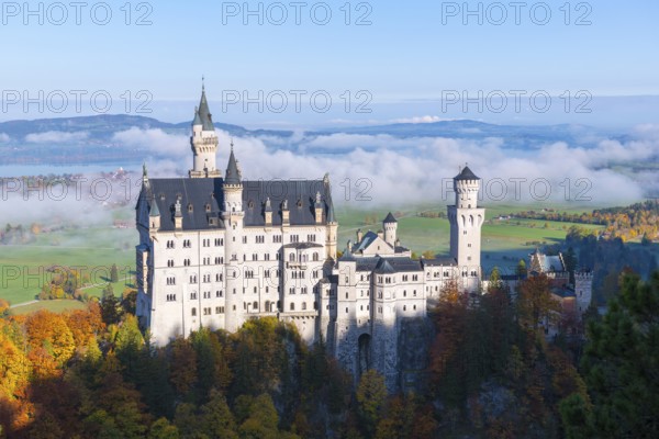 Dream castle Neuschwanstein towers over a fog-covered valley, surrounded by colorful autumn forest