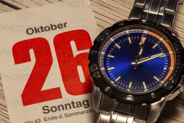 Wintertime 2025 time change: Close-up of a wristwatch and a sheet of a tear-off calendar showing