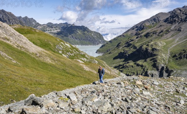 Hiker in a wide mountain landscape with a view of valley and lake, surrounded by green hills, Mont