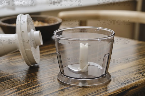 A clear food processor bowl on a rustic wooden table, ready for use. Nearby, the processor's motor