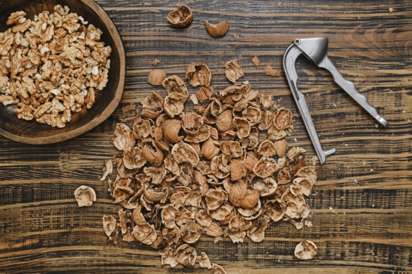 Walnuts are being shelled on a rustic wooden surface. A bowl of walnut pieces sits nearby, while